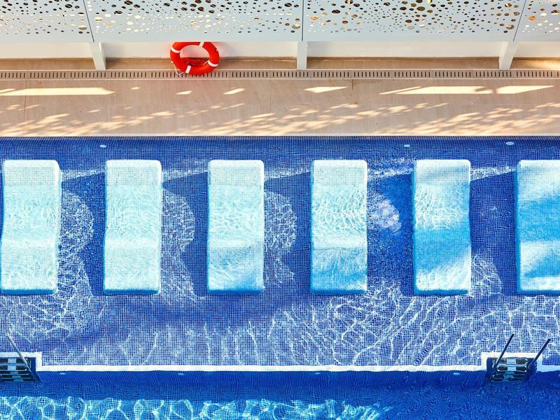 Zes witte ligstoelen op een rij in een blauw zwembad met een reddingsboei op het terras.