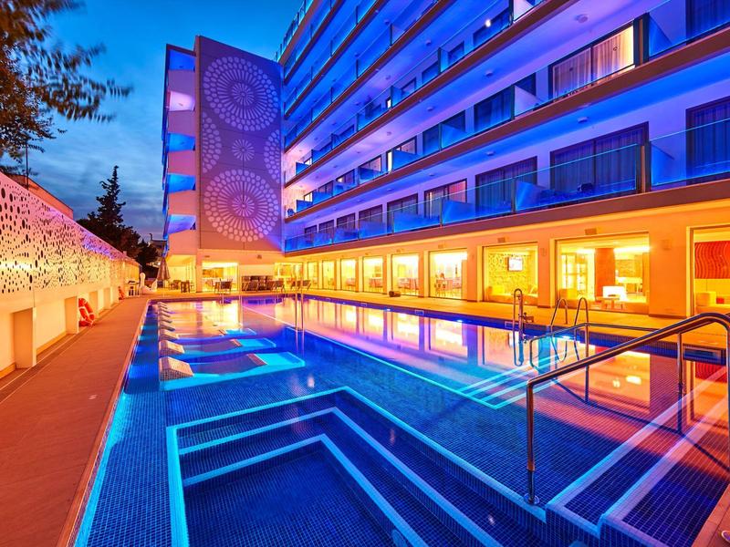 Hotelzwembad bij schemering met blauwe verlichting en verlichte moderne gevel.