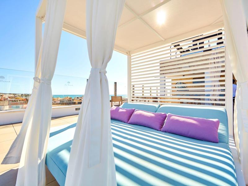 Moderne buitenlounge met blauwe matras en paarse kussens onder wit baldakijn op zonnig terras.