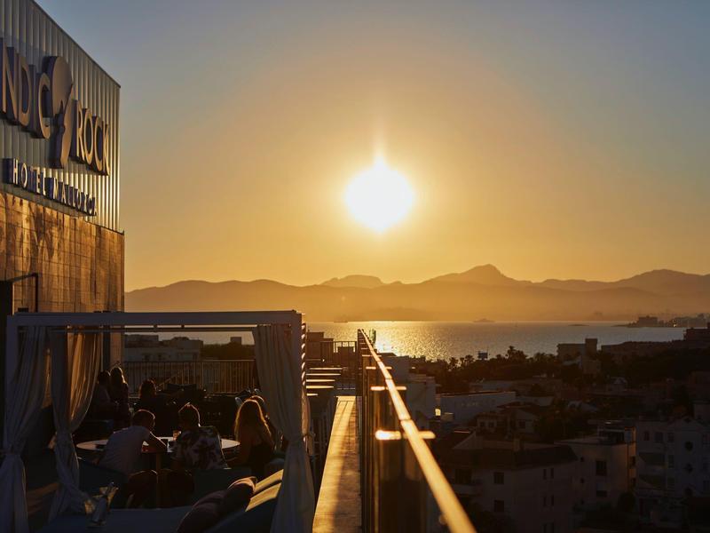 Zonsondergang uitzicht vanaf een hotelterras over een kuststad en bergen.