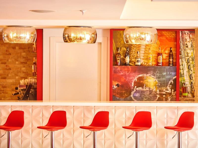 Moderne hotelbar met vijf rode stoelen en drie gouden hanglampen.