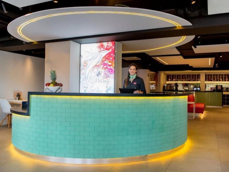 Nowoczesna recepcja hotelowa z okrągłym, niebiesko-zielonym kontuarem i stylowym oświetleniem.