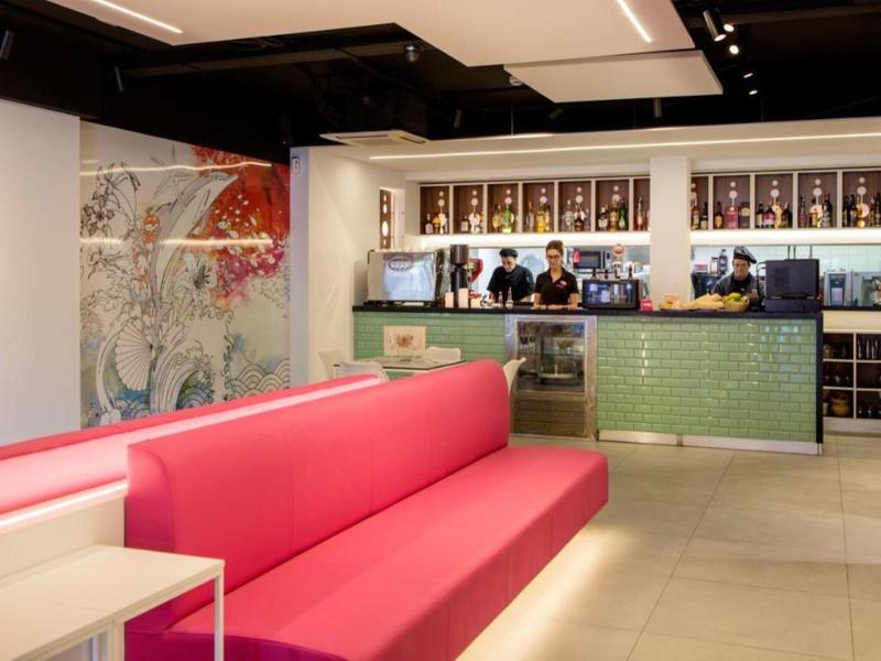 Nowoczesna strefa lounge hotelowa z czerwonym sofą i barem w tle.