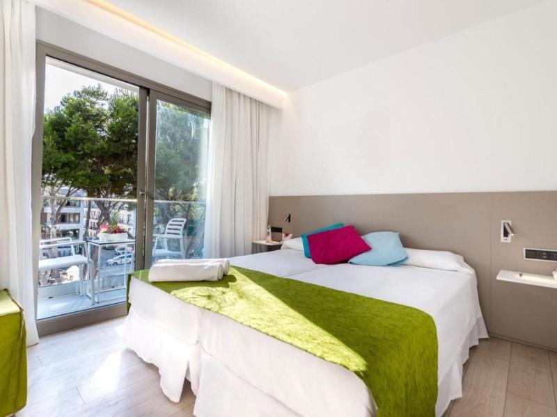 Jasny pokój hotelowy z podwójnym łóżkiem, kolorowymi poduszkami i widokiem na ruchliwą ulicę.