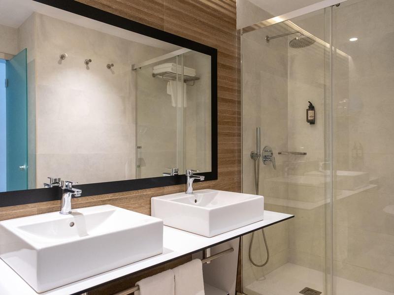 Nowoczesna łazienka z dwoma umywalkami, dużym lustrem i szklaną kabiną prysznicową.