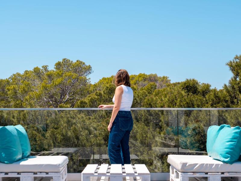 Kobieta cieszy się widokiem drzew z tarasu z białymi meblami i niebieskimi poduszkami.