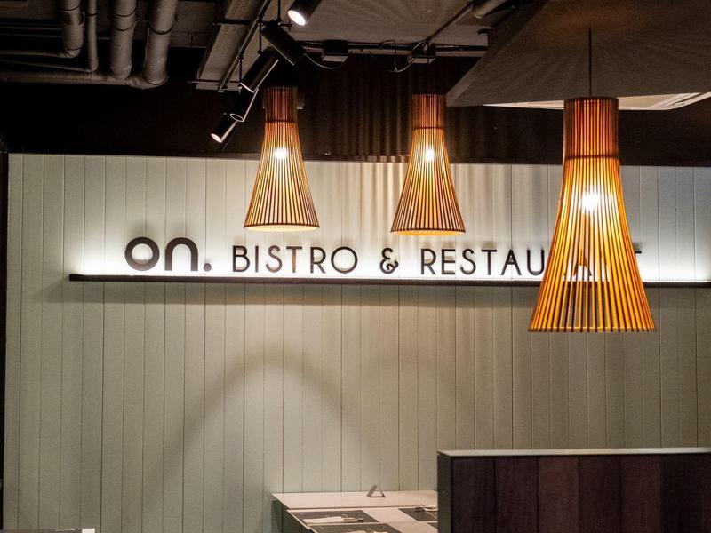 Przytulny kącik bistro z wiszącymi lampami i nakrytymi stołami w ciepłych kolorach.