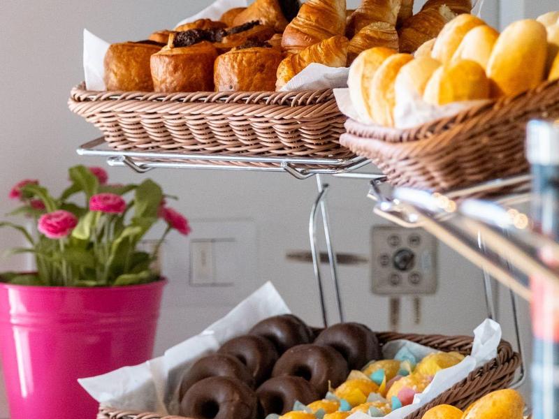 Różne świeże wypieki w koszach na bufecie z różowym doniczkiem z kwiatami w tle.