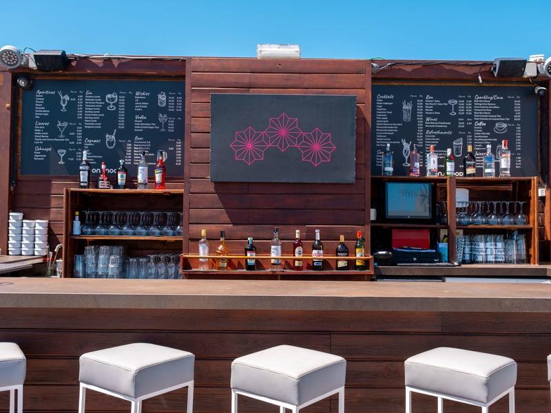 Bar na zewnątrz z drewnianymi panelami, alkoholami i stołkami pod bezchmurnym niebem