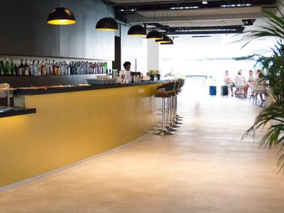 Area bar moderna in hotel con bancone giallo, sgabelli alti e lampade a sospensione.