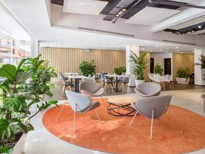 Modernes, helles Büro mit Pflanzen, grauen Stühlen und rundem orangefarbenem Teppich.