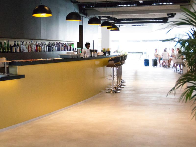 Area bar moderna in hotel con bancone giallo, sgabelli alti e lampade a sospensione.