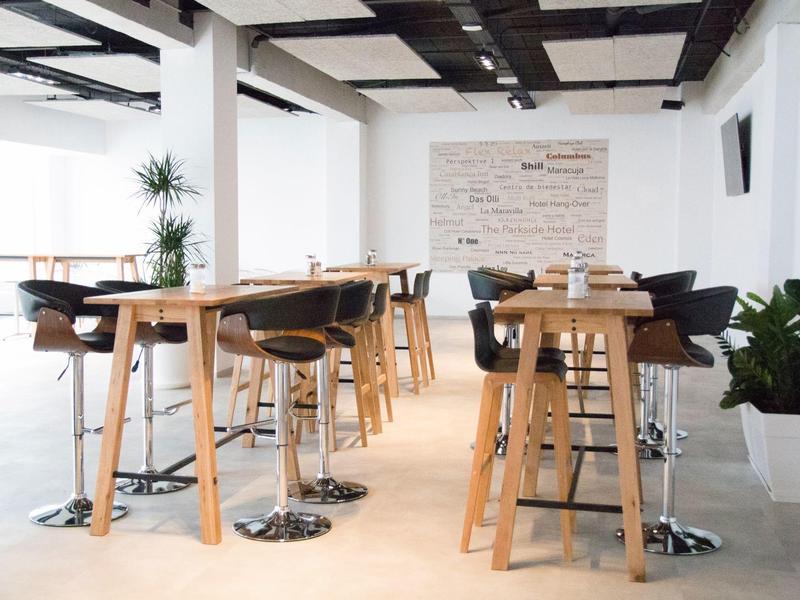 Area pranzo moderna con tavoli alti in legno e sedie nere in una stanza luminosa