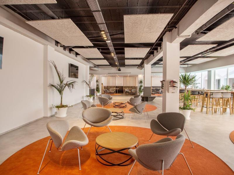 Area lounge aperta dell'hotel con sedie moderne e tavoli su tappeti arancioni.