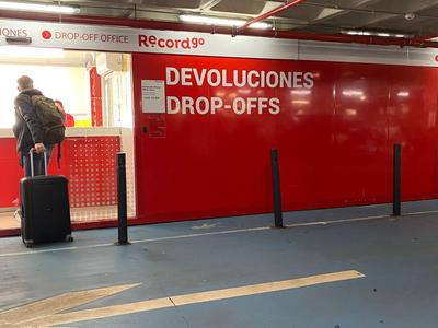 Persona con valigia con ruote al banco di restituzione rosso in un parcheggio.