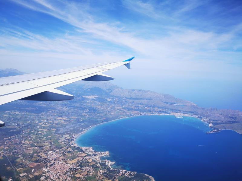 Výhled z okna letadla na pobřeží, moře a zamračenou oblohu.