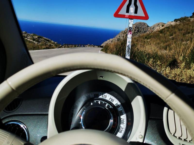 Vista dal sedile del conducente sul cruscotto con strada e cartello stradale davanti.