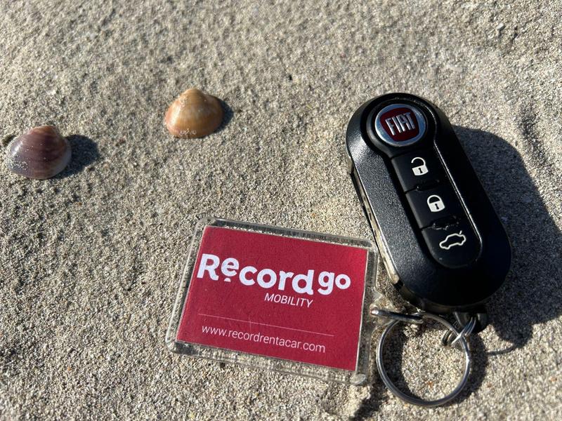 Chiave dell'auto e carta Recordgo Mobility sulla sabbia con conchiglie