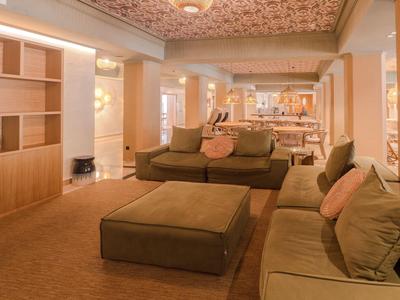 Moderní hotelový salonek se zelenými pohovkami a teplým osvětlením.