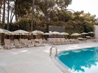 Pool area with lounge chairs and white umbrellas next to an outdoor hotel setting.