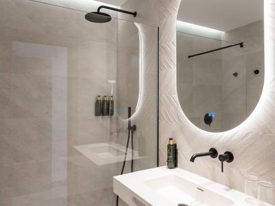 Modern hotel bathroom with walk-in shower, large illuminated mirror, and washbasin.