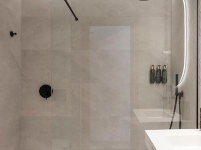 Modern hotel bathroom shower with large gray tiles and black showerhead.