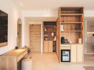 Modern hotel corridor with wooden furniture, minibar, coffee maker, and a wall-mounted TV.