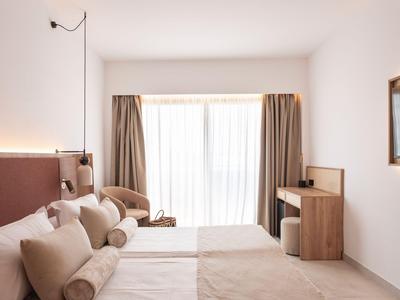 Simple hotel room with two single beds, soft pillows, and large windows with curtains.
