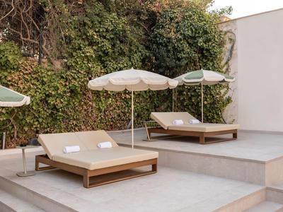 Two wooden loungers with white towels and umbrellas on a terrace with a green wall in the background.