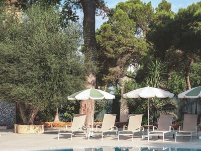 A calm pool area with lounge chairs and umbrellas surrounded by green trees.
