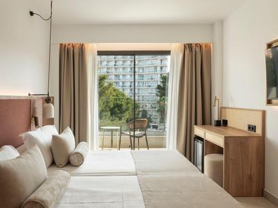Modern hotel room with two beds and balcony overlooking city buildings.