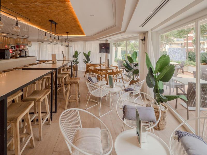 Světla, moderní hotelová restaurace s barem, dřevěnými židlemi a odpočinkovou zónou s bílými židlemi.