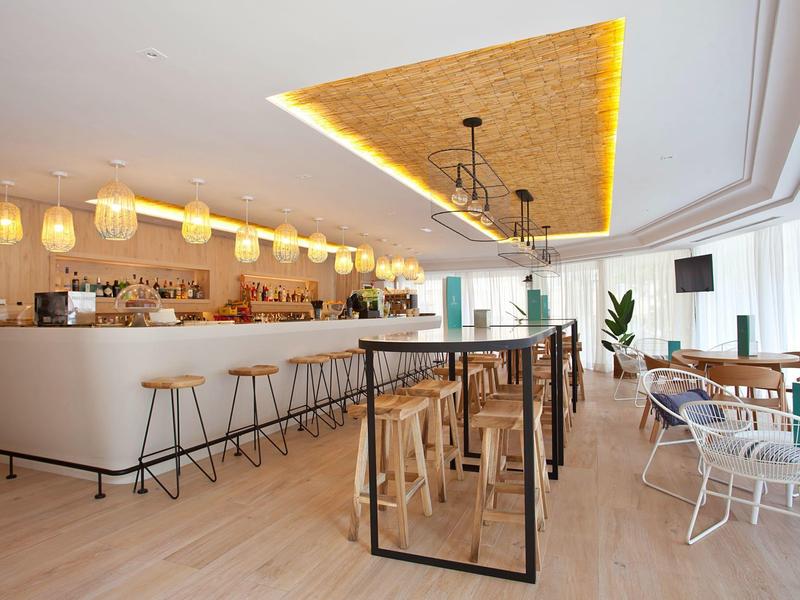 Světla restaurace s barem, dřevěnými a kovovými stoličkami, moderním designem a velkými okny.