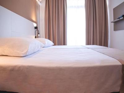 Camera d'hotel moderna con un grande letto, lenzuola bianche e tende.