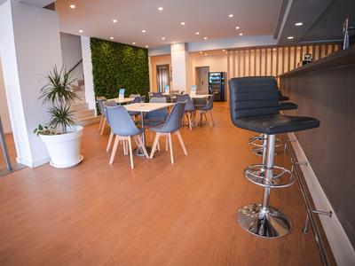 Nowoczesna przestrzeń lounge w hotelu z drewnianą podłogą, roślinami, stolikami, krzesłami i hokerami