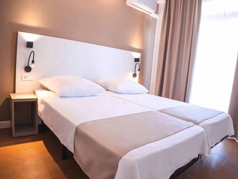 Pokój z dwoma pojedynczymi łóżkami, szafkami nocnymi i zasłonami w świetle dziennym.