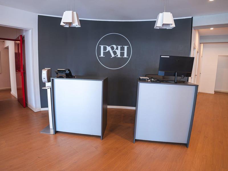 Nowoczesna recepcja z dwoma ladami na tle ciemnej ściany z logo hotelu.