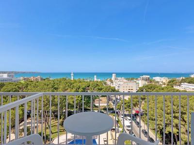 Balcon avec table donnant sur des arbres, des bâtiments et la mer à l'horizon.