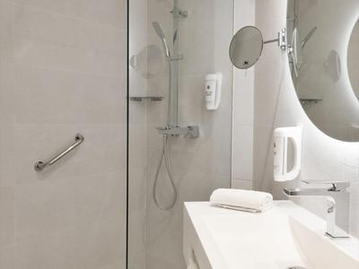 Salle de bain moderne avec douche à l'italienne, grand miroir et lavabo blanc.