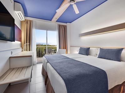 Nowoczesny pokój hotelowy z podwójnym łóżkiem, balkonem i widokiem na zieleń.