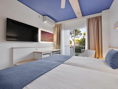 Chambre d'hôtel moderne avec grand lit, télévision à écran plat et balcon donnant sur des palmiers.