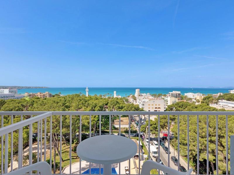Balcon avec table donnant sur des arbres, des bâtiments et la mer à l'horizon.