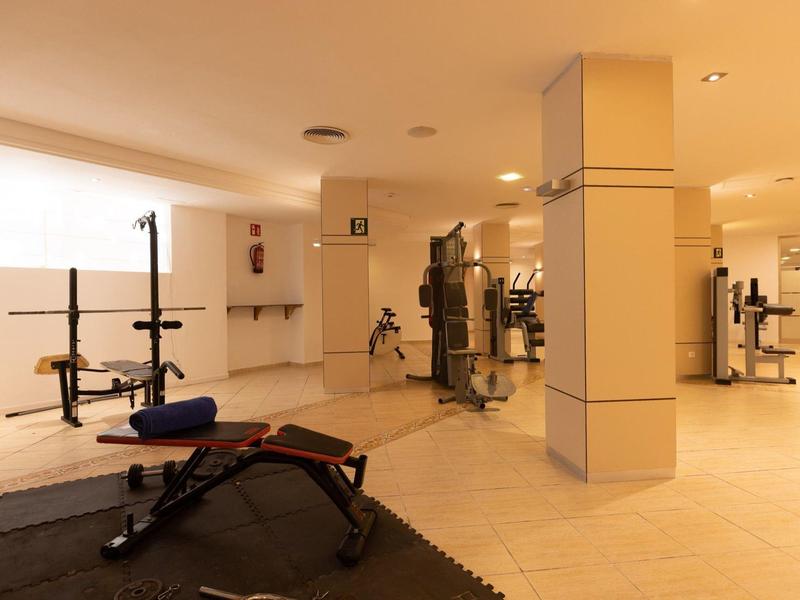 Salle de sport bien éclairée avec machines et poids libres sur sol carrelé dans un hôtel.