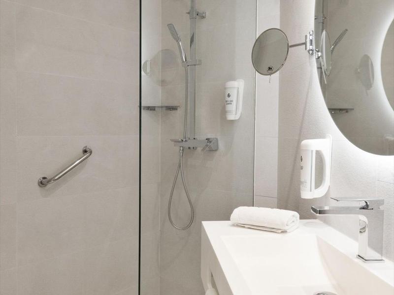 Salle de bain moderne avec douche à l'italienne, grand miroir et lavabo blanc.