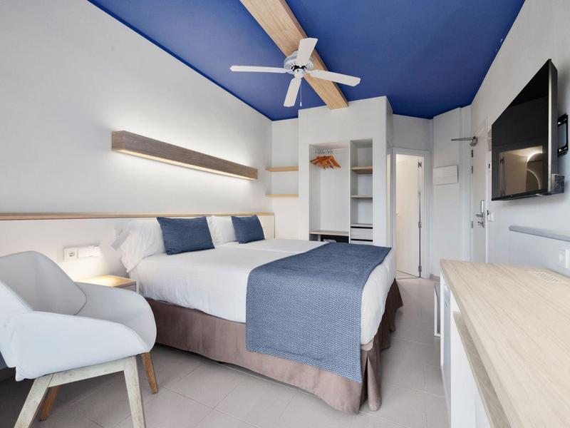 Chambre d'hôtel moderne avec accent de plafond bleu, lit double et fauteuil confortable.