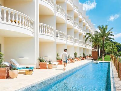 Hombre caminando junto a una piscina de hotel con balcones tipo balaustrada y palmeras.