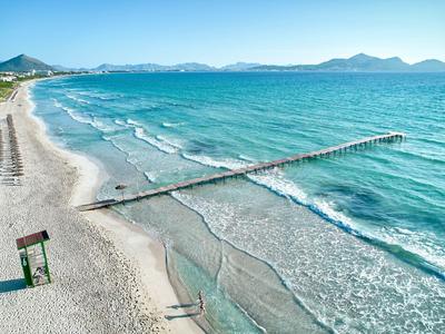 Una lunga passerella si estende sul mare blu chiaro su una spiaggia sabbiosa soleggiata.