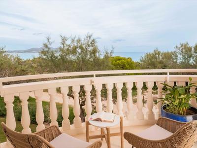 Balcone con sedie, tavolo e piante con vista sul mare e sugli alberi.