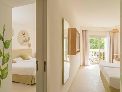 Camera d'hotel luminosa con due letti, balcone e stanza adiacente con letto singolo.