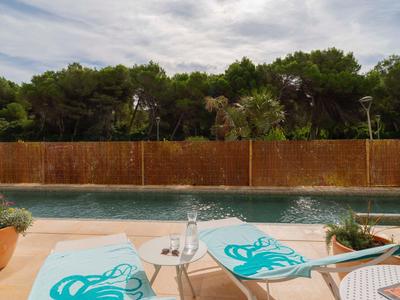 Due sdraio con cuscini blu vicino a una piscina davanti a una recinzione di legno e alberi.